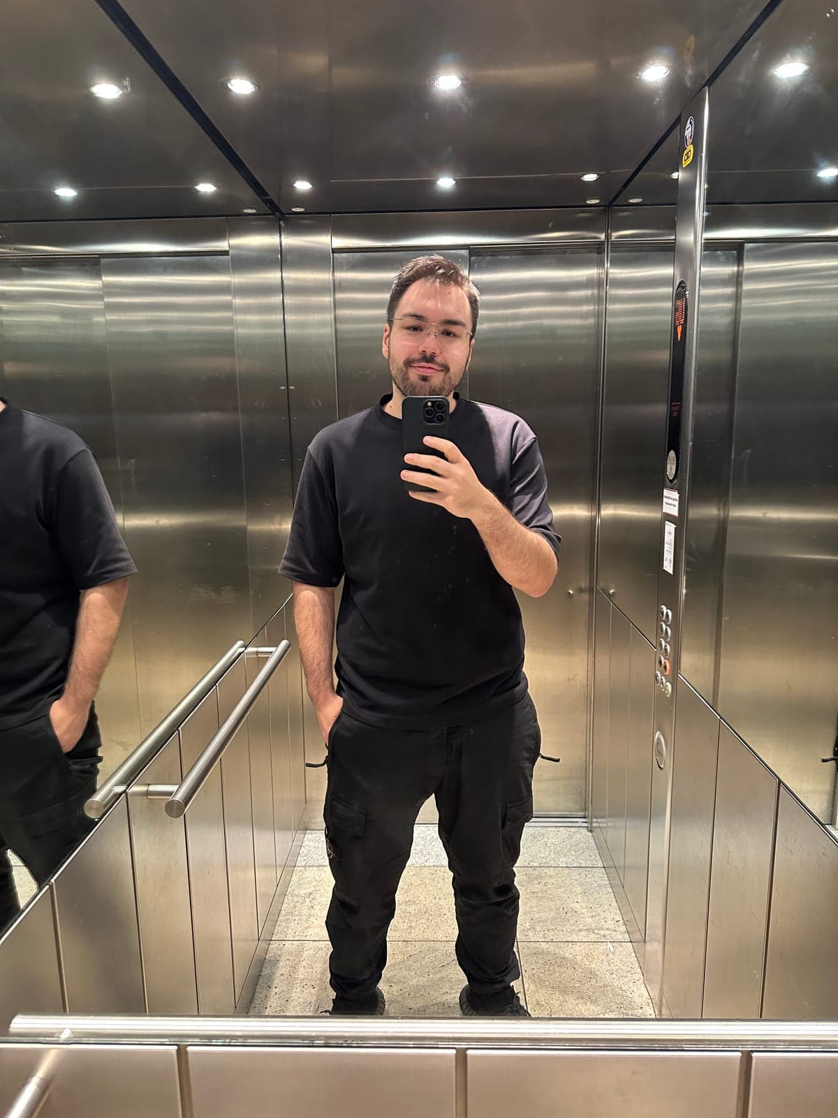 Dennis heute: Ganzkörper-Spiegel-Selfie im Aufzug, schwarzes T-Shirt, deutlich schlanker