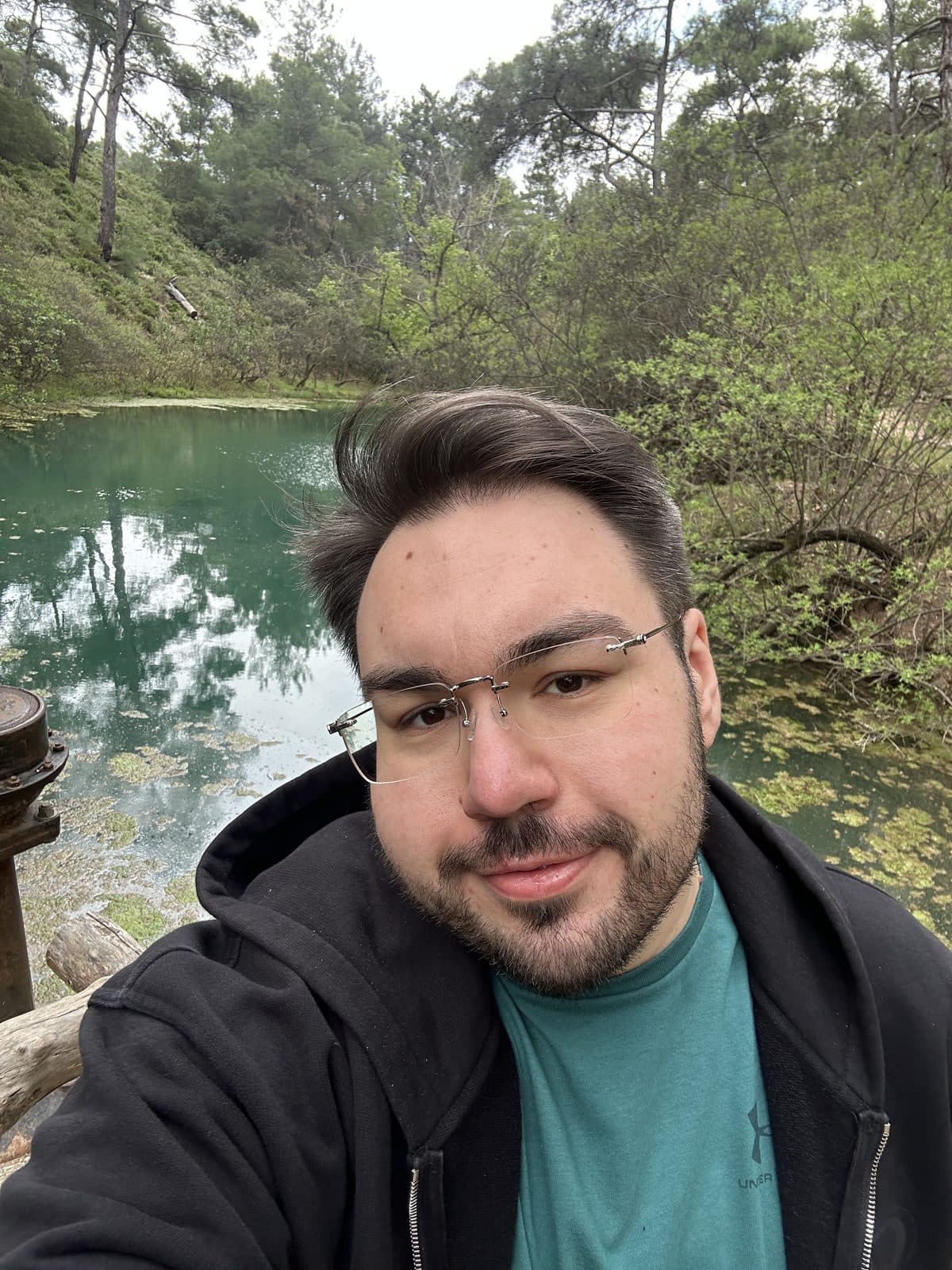 Dennis heute: Selfie am See im schwarzen Hoodie, schaut direkt in die Kamera
